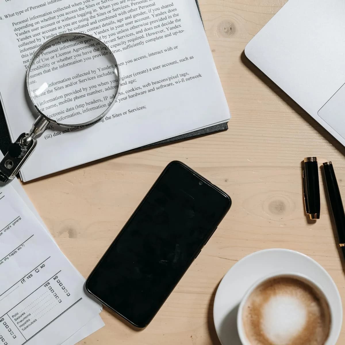 Top-down desk scene with paperwork, a laptop, coffee, and office stationery.